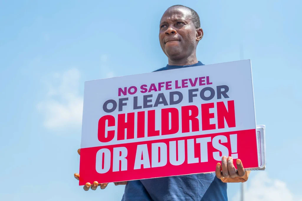 A protestor holds up a sign that says "NO SAFE LEVEL OF LEAD FOR CHILDREN OR ADULTS"