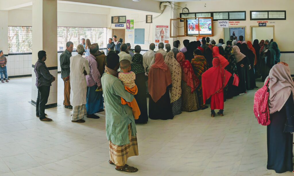Patients queueing in a bright room with a tiled floor. 46 people are visible, and the queue disappears through a pair of doors