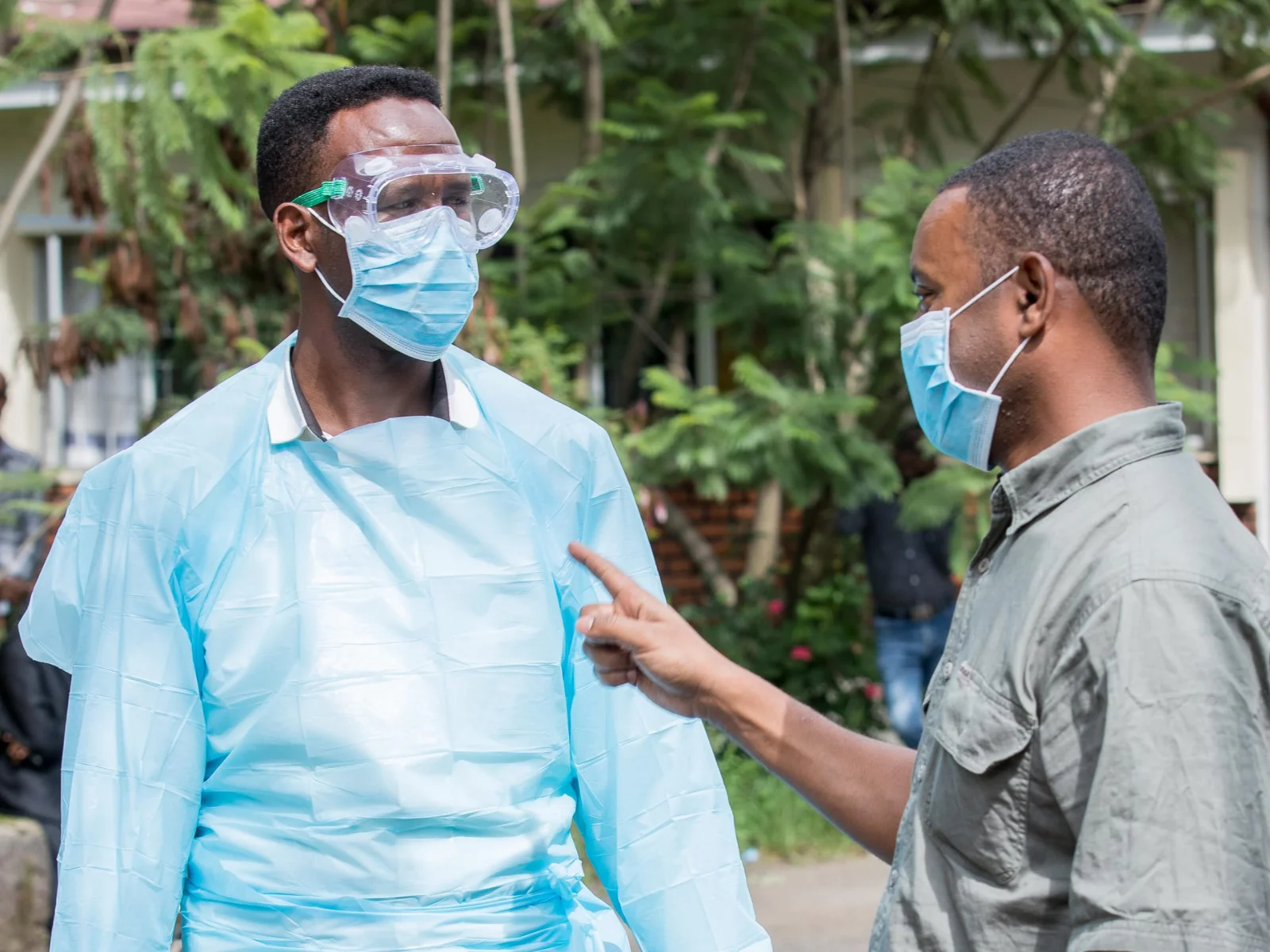 A African heathcare worker in PPE, with mask and goggles, is being pointed at by another man in a mask during PPE training