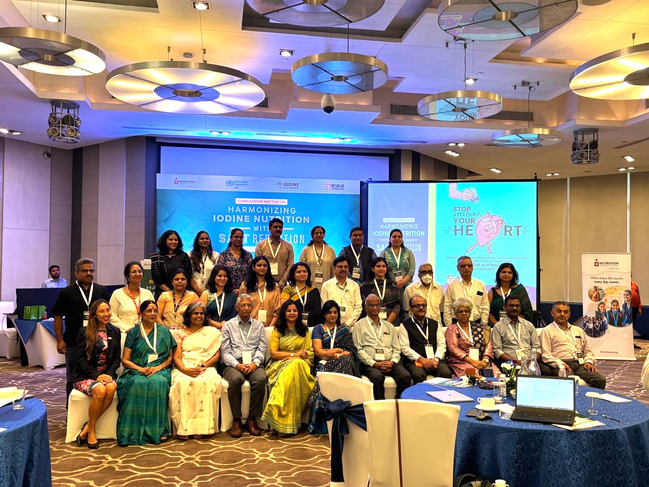 conference room group photo with members from RTSL, Nutrition International, WHO India, and the Iodine Global Network in the forefront and projector screen with title slide in the background