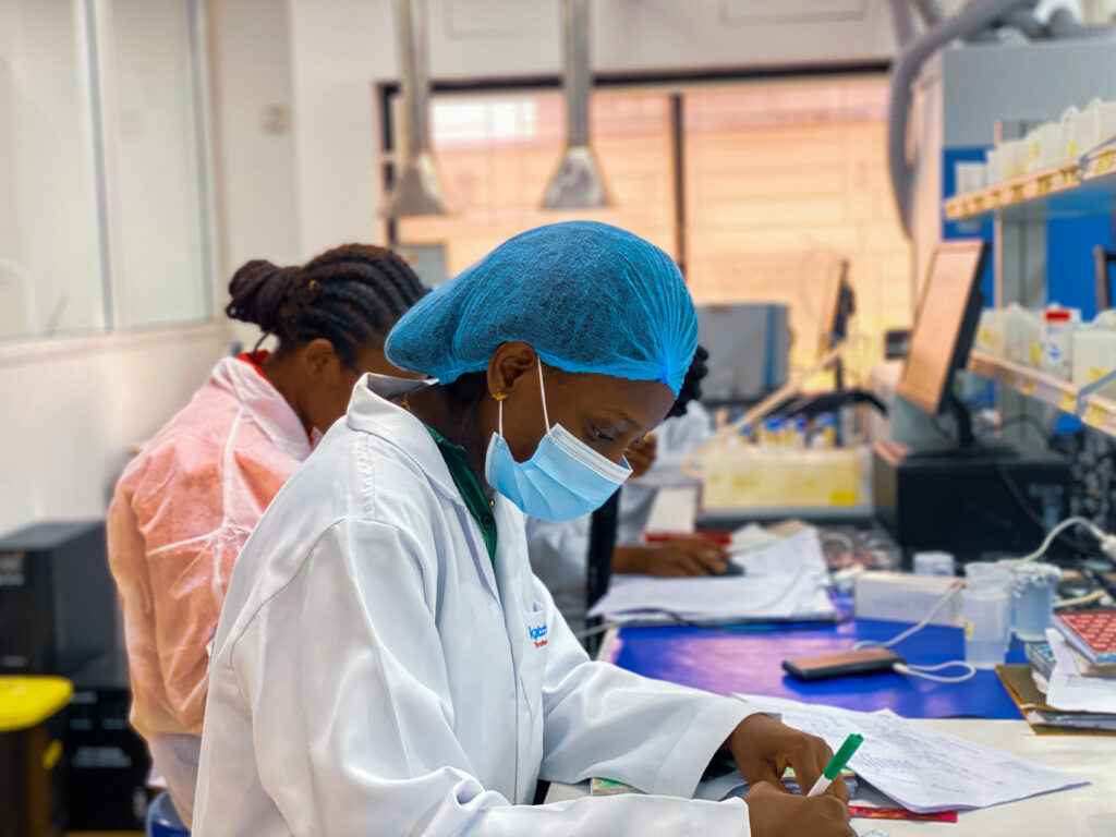 trans fat lab techs sitting at laboratory table with white lab coat and blue head cap and mask