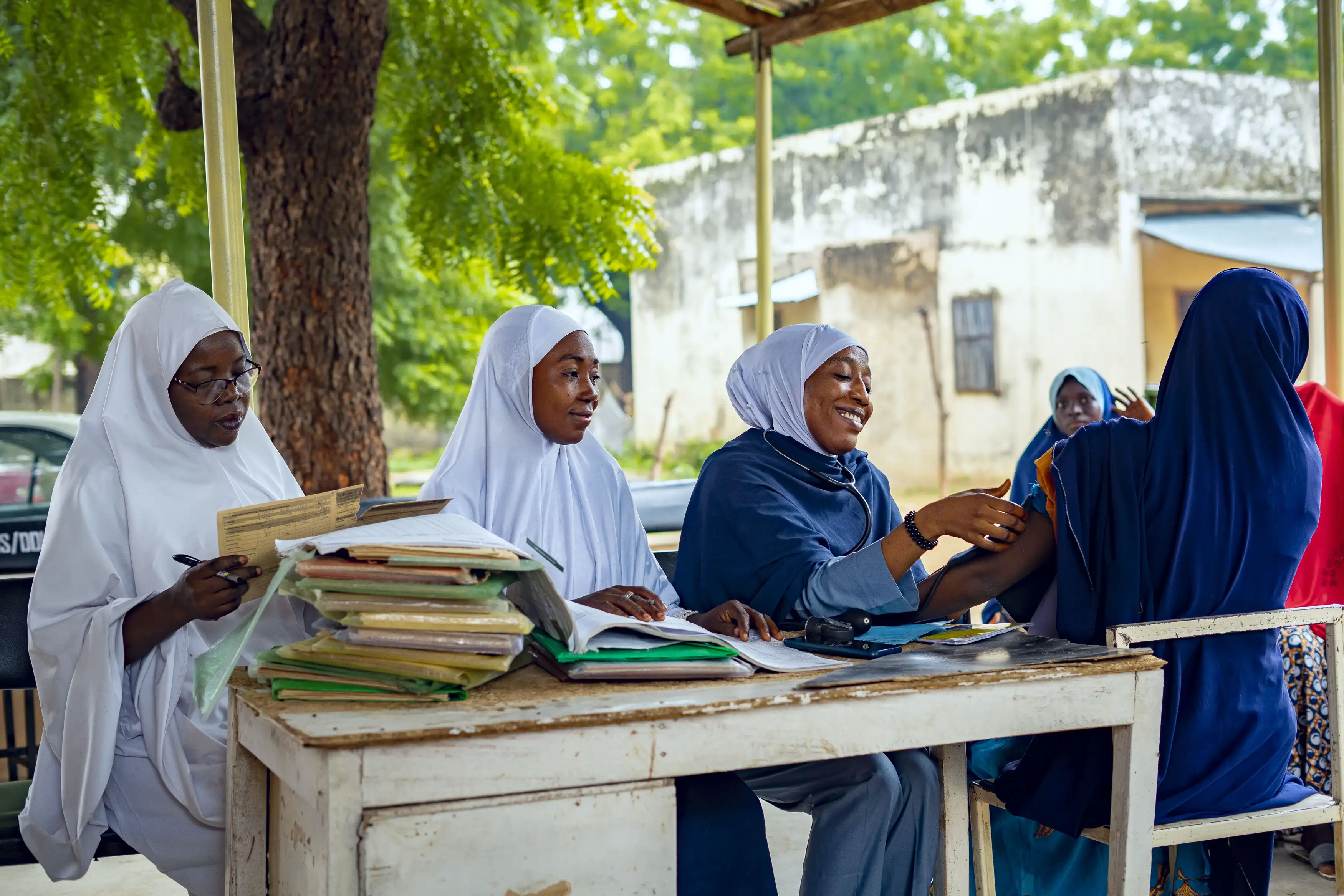In Kano State, Nigeria, community health care workers take patients' blood pressure measurements outdoors on a sunny day.