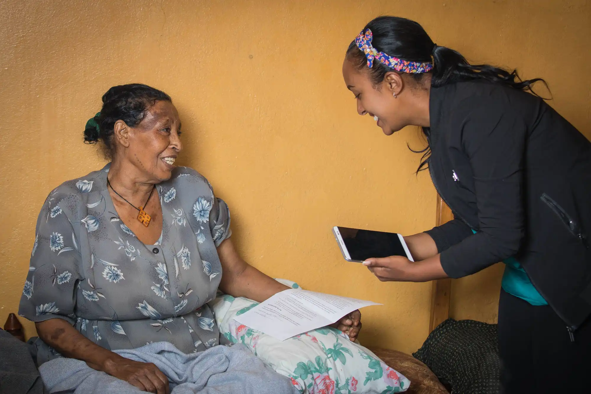 A smiling researcher with an ipad speaks to a seated, smiling woman in the Ethiopia Salt Consumption KAP survey in February 2020, in Addis Ababa.