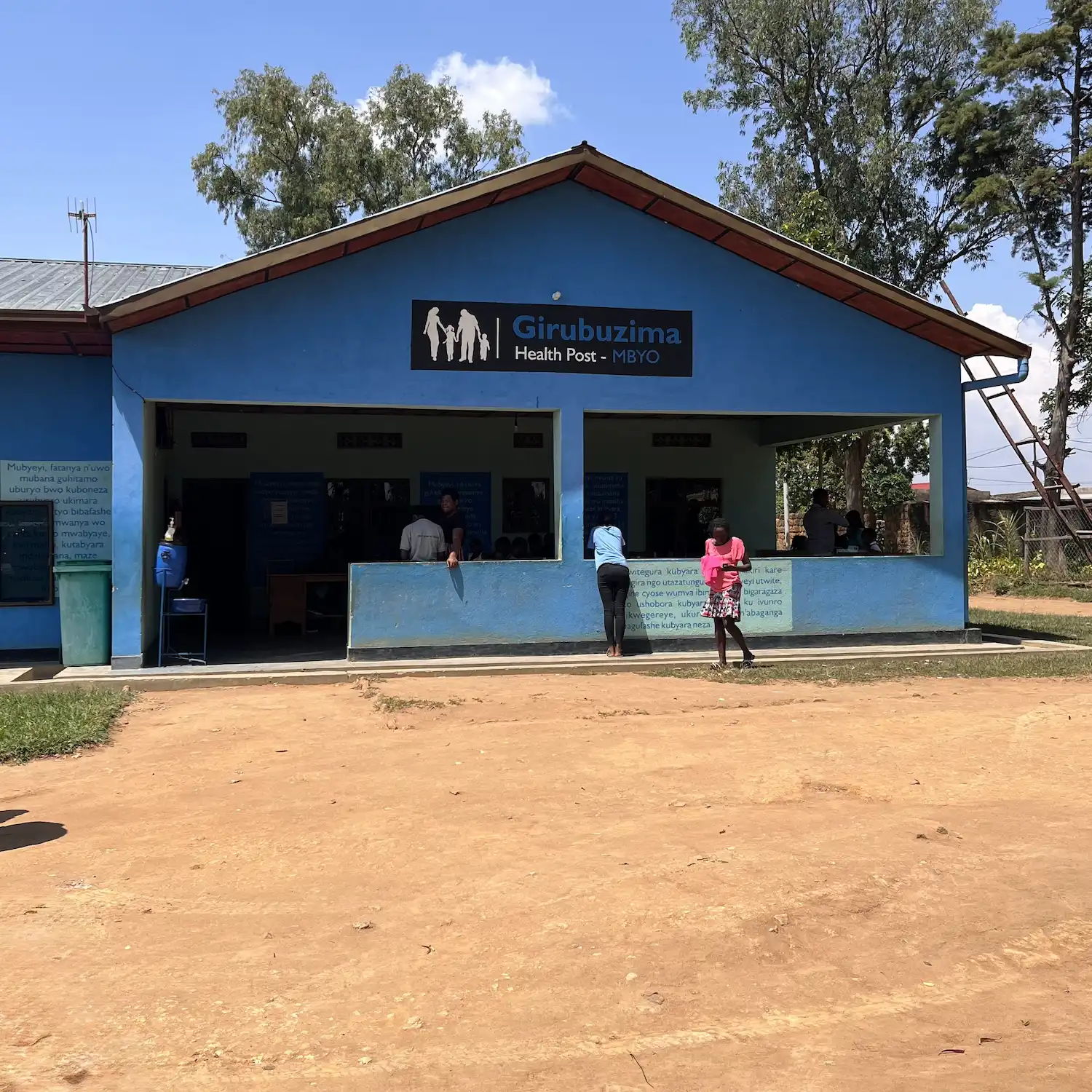 A blue painted building on dusty ground, with a sign outside that says Health Post