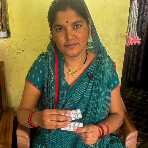 An Indian woman holding up her blood pressure medication to the camera