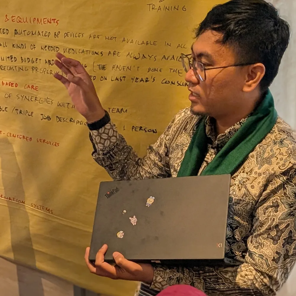 An Asian man holding a laptop and talking to a group off camera