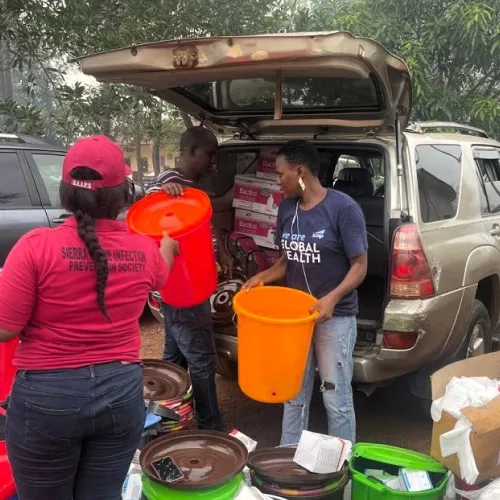 A female African Health Care worker, standing outside in the sun, smiling at the camera